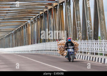 Motorradfahrer, die durch die Kahayan-Brücke fahren und Ladungen in Palangkaraya, Zentral-Kalimantan, Indonesien tragen. Stockfoto