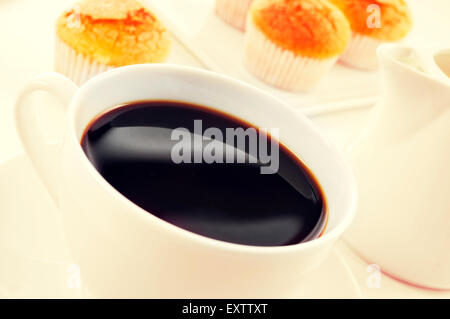 Nahaufnahme von einer Tasse Kaffee und einem Haufen von Magdalenas, die typisch spanische schlicht Muffins, in einem weißen Teller auf einem gedeckten Tisch, filtere Stockfoto