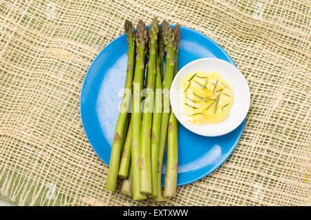 Reihe von frischem Spargel und Butter Dip mit Rosmarin auf eine blaue Platte mit Hanf Tischdecke gelegt. Stockfoto