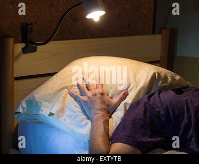 Junger Mann auf dem Bett mit einem Kissen über den Kopf Stockfoto