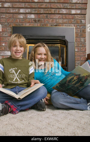 Junge und Mädchen genießen Lesung vor einem Gaskamin im Familienzimmer.  Konzepte: informelle Bildung, lernen Stockfoto