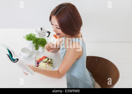 Junge Frau essen Salat und ein Buch hält, Stockfoto