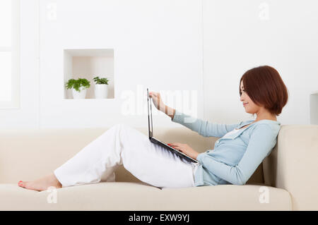 Junge Frau auf dem Sofa sitzen und mit Laptop, Stockfoto
