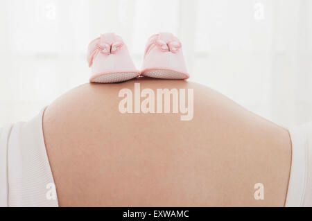 Ein paar Babyschuhe auf schwangere Frau Bauch, Stockfoto