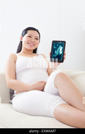 Schwangere Frau sitzen und halten Touch-Pad mit Lächeln, Stockfoto