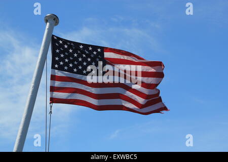 Amerikanische Flagge, zeigt die volle Sterne und Streifen auf einem weißen Fahnenmast im Wind vor blauem Himmel Stockfoto