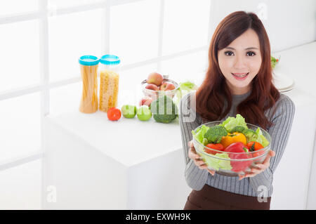 Junge Frau hält Gemüse und lächelt in die Kamera, Stockfoto