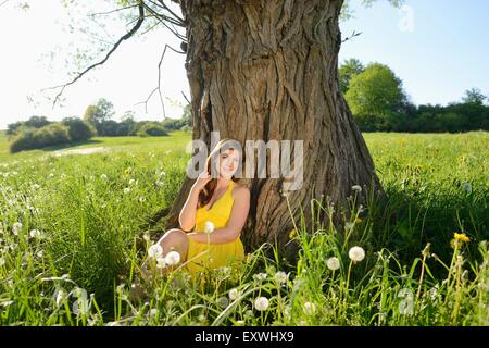 Junge Frau sitzt an einem Baum, Bayern, Deutschland, Europa Stockfoto