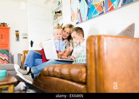 Mutter mit Kindern (4-5, 6 und 7) mit Laptop auf Sofa Stockfoto