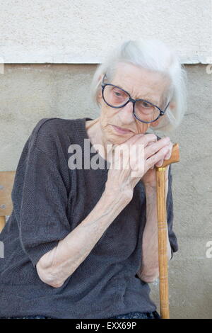 Porträt von einem neunzig Jahre alt Oma stützte sich auf einen Gehstock beim Sitzen im freien Stockfoto