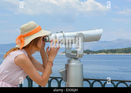 Junges Mädchen Blick durch öffentliche Fernglas am Meer mit Stroh Hut und rosa Kleid Stockfoto