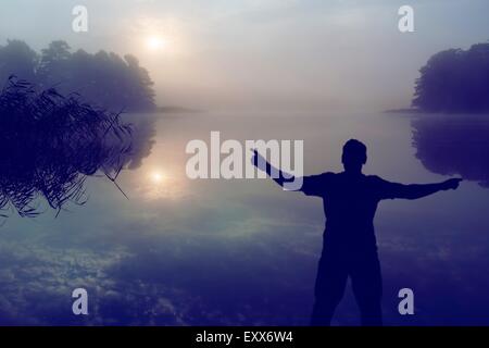 Mann einen Sonnenaufgang über See zu beobachten. Menschliche Silhouette. Foto mit Vintage Stimmung Wirkung. Stockfoto