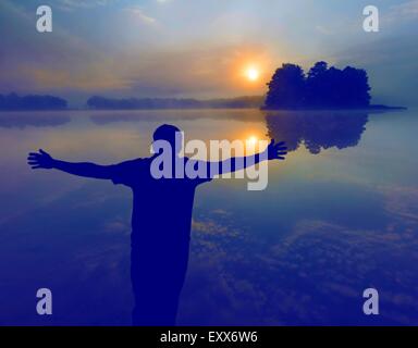 Mann einen Sonnenaufgang über See zu beobachten. Menschliche Silhouette. Foto mit Vintage Stimmung Wirkung. Stockfoto