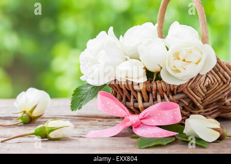 Weidenkorb mit wilden Rosen-Blumen und rosa Schleife. Hochzeit oder Geburtstag Dekoration im rustikalen Stil. Stockfoto
