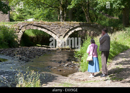 Älteres Ehepaar stand neben Lastesel Brücke über Wycoller Beck, Wycoller, Lancashire Stockfoto