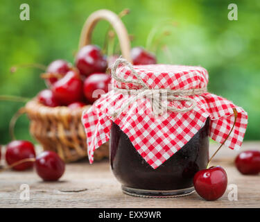 Gläser Marmelade und Korb mit Kirsche auf Hintergrund. Stockfoto