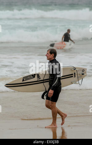 Zwei Männer Fuß Oppisite Richtungen mit ihren Surfbrettern an einem Strand in Newcastle.    Bildnachweis: Euan Cherry Stockfoto