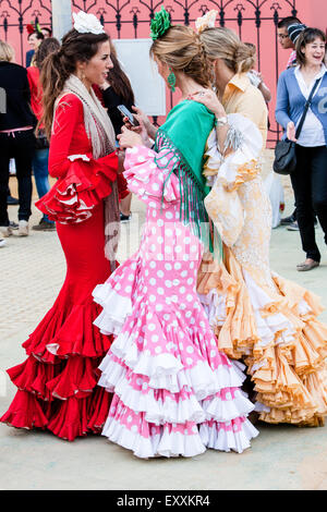 Junge Frauen mit Handy während des Tragens traditionelle Sevilla kleiden sich in Sevilla, Andalusien, Spanien, Europa. Auf April Feria Festival. Stockfoto