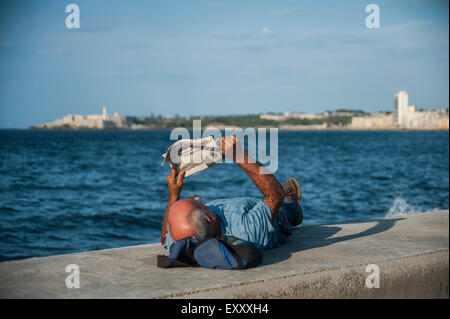 Ein Mann liest die Zeitung und entspannt entlang der Ufermauer und Malecon in Havanna, Kuba Stockfoto