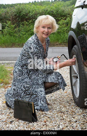 Ältere Frau bereitet sich der Reifendruck auf ihrem Auto Reifen Druckprüfung eines Fahrzeugs mit einem Messgerät prüfen Stockfoto
