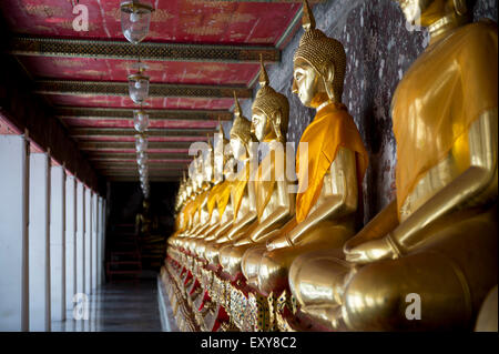 Reihe von Golden sitzenden Buddhas tragen gelbe Schärpe vor dekorative Wand in einem buddhistischen Tempel in Bangkok Thailand Stockfoto