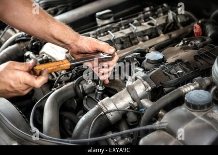 Mechaniker mit einem Schraubenschlüssel und Sockel auf dem Motor eines Kraftfahrzeugs Stockfoto