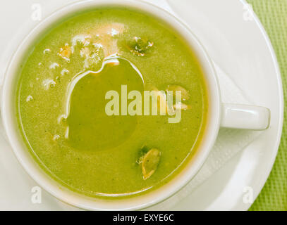 Hausgemachte Broccoli-Suppe mit Kürbiskernen in einer kleinen Schüssel auf weißen Teller und grünem Hintergrund Stockfoto