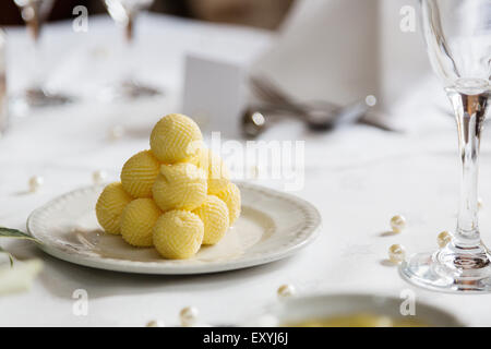 Eine Pyramide von gelben Butter Kugeln auf ein gedeckter Tisch für ein Bankett. Die Kugeln werden auf Teller mit frischen Brötchen verwendet werden serviert. Stockfoto