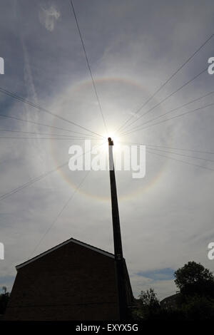 Epsom, Surrey, UK. 18. Juli 2015. Wie ein Tal der dünnen Wolke über den Himmel und mit einem Telegrafenmast blockieren die volle Leuchtkraft der Sonne treibt, ist ein Halo sichtbar in den Himmel. Die Rundschreiben (oder 22 Grad) Halo ist ein optisches Phänomen, produziert von Licht, die Interaktion mit Eiskristallen in der Atmosphäre, ein Regenbogen-Effekt um die Sonne ausgesetzt. Bildnachweis: Julia Gavin UK/Alamy Live-Nachrichten Stockfoto