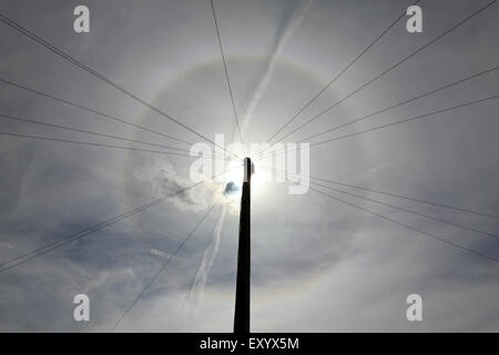 Epsom, Surrey, UK. 18. Juli 2015. Wie ein Tal der dünnen Wolke über den Himmel und mit einem Telegrafenmast blockieren die volle Leuchtkraft der Sonne treibt, ist ein Halo sichtbar in den Himmel. Die Rundschreiben (oder 22 Grad) Halo ist ein optisches Phänomen, produziert von Licht, die Interaktion mit Eiskristallen in der Atmosphäre, ein Regenbogen-Effekt um die Sonne ausgesetzt. Bildnachweis: Julia Gavin UK/Alamy Live-Nachrichten Stockfoto