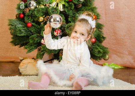 Das dreijährige Mädchen in ein neues Jahr Kleid sitzen auf einer Matte am Weihnachtsbaum Stockfoto