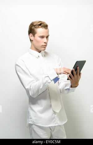 Ein hübscher junger Mann hält ein Ipad/Tablet, wegschauen. Er trägt eine schneeweiße Outfit, eine saubere futuristisches Konzept Stockfoto