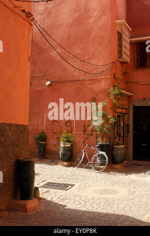 Rotes Fahrrad, das sich an orangefarbene Wände, hintere Straßen, Marrakesch, Marokko anlehnt Stockfoto