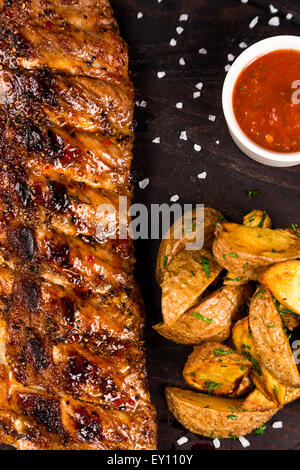 Bbq Ribs mit Braten Kartoffeln und Sauce auf dunklem Holz geröstet Stockfoto