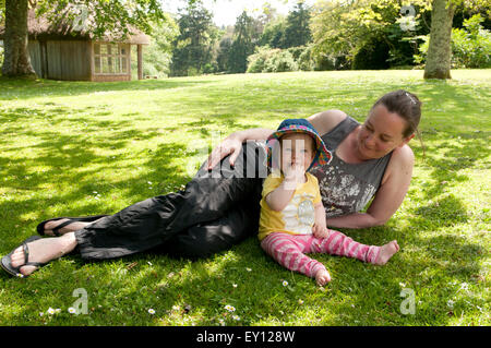 Mutter liegt auf dem Gras mit ihrem Baby Mädchen im Garten an einem schönen Sommertag Stockfoto