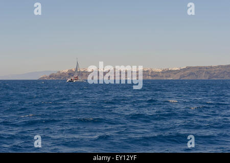 Ein Katamaran-Segeln in das tiefblaue Meer und die weißen Häuser auf der Caldera in der Ferne, Santorini, Griechenland. Stockfoto