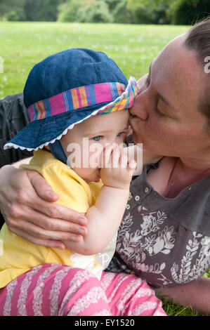 Babymädchen saugen ihre Daumen und getröstet von der Mutter in den Garten Stockfoto