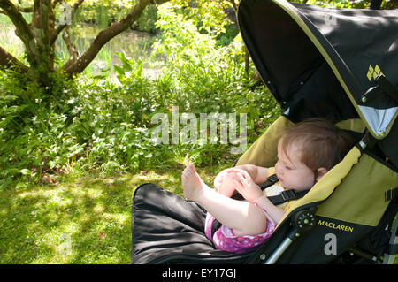 Babymädchen in ihrem Kinderwagen im Freien spielen mit ihren Füßen Stockfoto