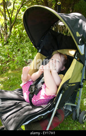 Babymädchen in ihrem Kinderwagen im Freien spielen mit ihren Füßen Stockfoto