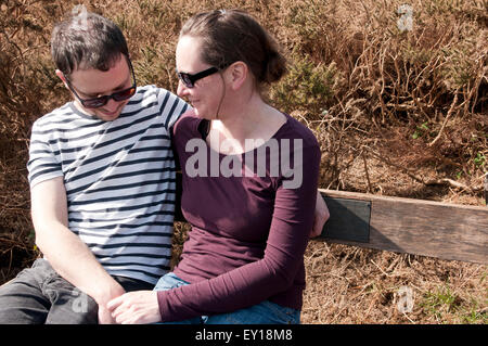 Paar mit ihre Arme umeinander sitzen auf einer Bank Stockfoto