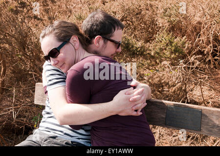 Paar mit ihre Arme umeinander sitzen auf einer Bank Stockfoto