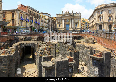 Überreste eines römischen Amphitheaters im Stadtzentrum von Catania mit reich verzierten Gebäude San Biago hinter. Sizilien, Italien