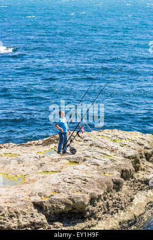 Einen einsamen Fischer Meeresangeln vom Felsen am Ufer mit langen Stangen, Portland Bill, Dorset, Südwest-England Stockfoto