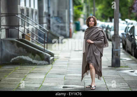 Junge attraktive Frau in einem Poncho steht auf der Straße in der Nähe des Hauses. Stockfoto