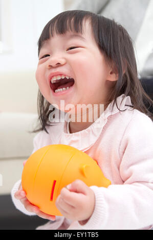 Babymädchen halten Sparschwein und glücklich lächelnd, Stockfoto