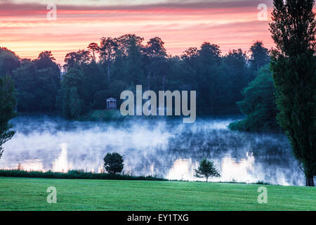 Sonnenaufgang über den dorischen Tempel und den See auf dem Gelände des Anwesens Bowood in Wiltshire. Stockfoto