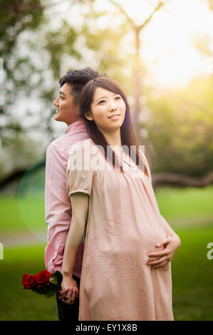 Schwangere und junge Mann stehend mit Rücken an Rücken und Hand in Hand, Stockfoto