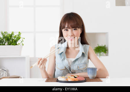 Junge Frau hält Sushi und lächelt in die Kamera, Stockfoto