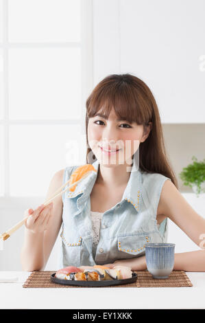 Junge Frau hält Sashimi und lächelt in die Kamera, Stockfoto