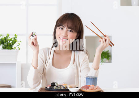 Junge Frau hält Sushi und lächelt in die Kamera, Stockfoto